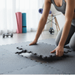 Close-up of hands interlocking grey foam floor tiles, showing the simple assembly process for home gym flooring.