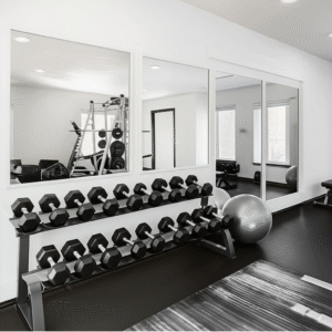 Large, frameless mirrors reflecting a clean, modern home gym with a dumbbell rack and workout equipment.